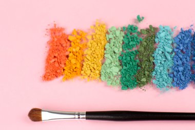 Gökkuşağı göz farı ve profesyonel makyaj fırçası pembe bir arka plan üzerinde ezilmiş