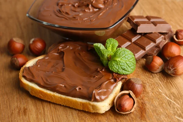 Pane con cioccolato dolce alla nocciola spalmato su fondo di legno — Foto Stock