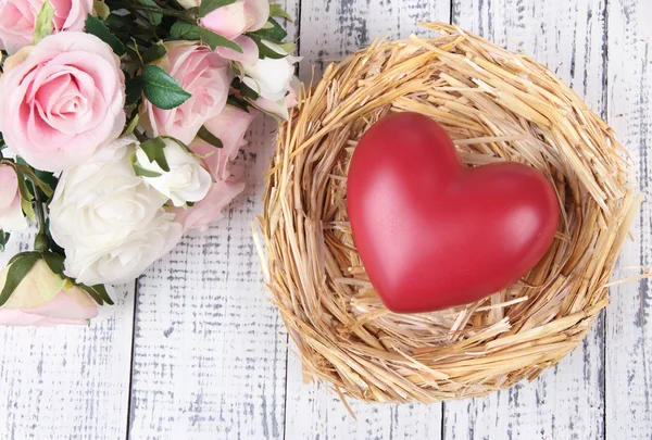 Decorative heart in nest, on color wooden background — Stock Photo, Image
