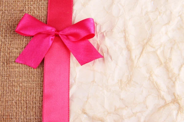 Sackcloth with color ribbon and bow on color paper background — Stock Photo, Image