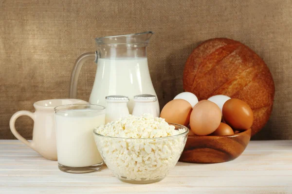 Tasty dairy products on wooden table, on sacking background — Stock Photo, Image