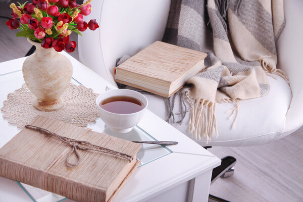 Состав с чашкой горячего напитка и печеньем на деревянном столе возле кресла
