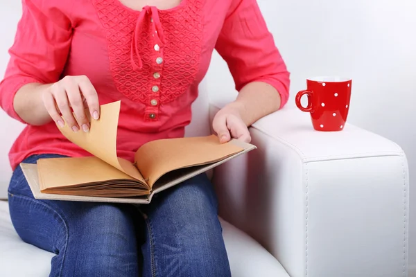 Kobieta siedzi na kanapie, czytanie książki i picia kawy lub herbaty, szczelnie-do góry — Zdjęcie stockowe