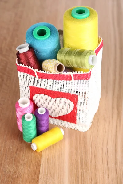 Bobine colorate di filo in borsa, su sfondo di legno — Foto Stock