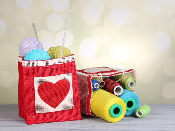 Bags with bobbins of colorful thread and woolen balls on wooden table, on light background — Stock Photo, Image
