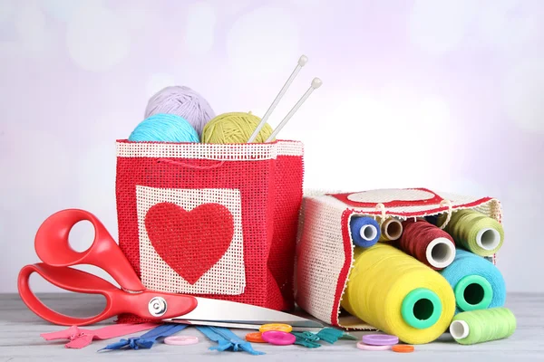 Tüten mit Spulen aus buntem Faden und Wollkugeln auf Holztisch, auf hellem Hintergrund — Stockfoto