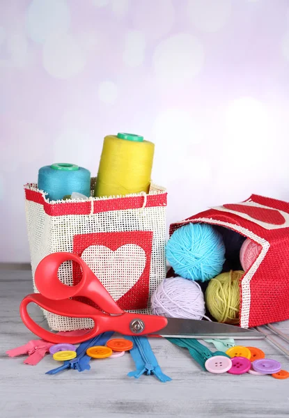 Bolsas con bobinas de hilo de colores y bolas de lana sobre mesa de madera, sobre fondo claro — Foto de Stock