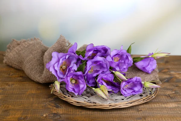 Purple artificial eustoma on sackcloth on color wooden  table, on bright background — Stock Photo, Image