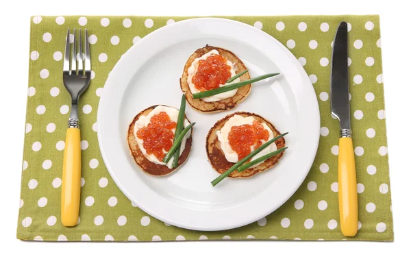 Pannenkoeken met rode kaviaar op plaat, op kleur servet, geïsoleerd op wit — Stockfoto