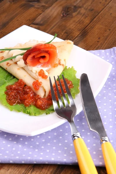 Блинчик с лососиной, красной икрой и майонезом, зеленый лук, на тарелке, на цветной салфетке, на деревянном фоне — стоковое фото
