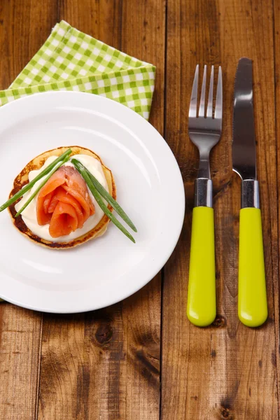 Pannkaka med lax och mayo, grön lök, på plattan, på färg Servett, på trä bakgrund — Stockfoto