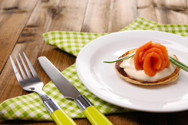Pancake con salmone e maionese, cipolla verde, su piatto, su tovagliolo di colore, su fondo di legno — Foto Stock