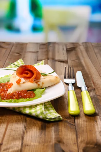 Pancake with red caviar, salmon and mayo, green onion, on plate, on color napkin, on wooden  table, on bright background — Stock Photo, Image