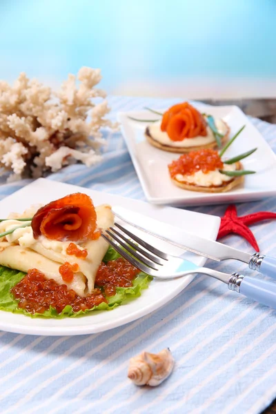 Panqueques con caviar rojo, salmón y mayonesa, cebolla verde, sobre plato, sobre servilleta de color, sobre mesa de madera, sobre fondo brillante —  Fotos de Stock