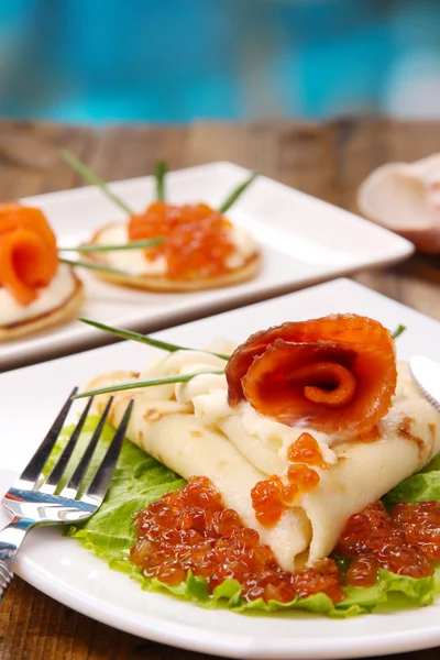 Panqueques con caviar rojo, salmón y mayonesa, cebolla verde, sobre plato, sobre mesa de madera, sobre fondo brillante — Foto de Stock