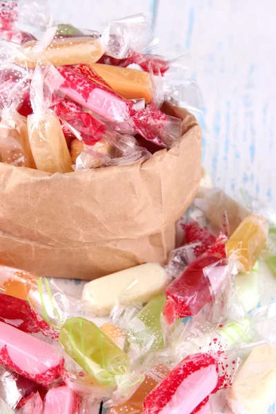 Tasty candies in paper bag on wooden background — Stock Photo, Image