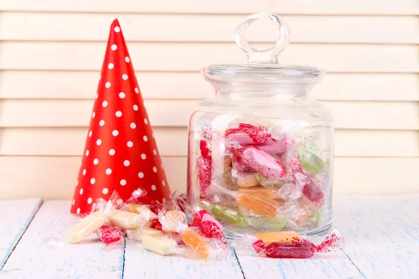 Tasty candies in jar with party hat on table on wooden background — Stock Photo, Image