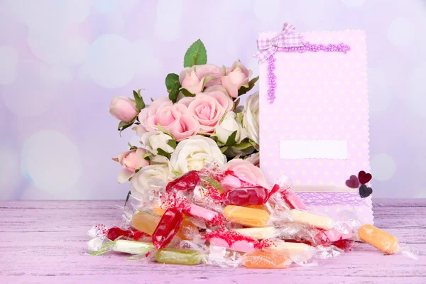 Tasty candies with flowers and card on table on bright background — Stock Photo, Image