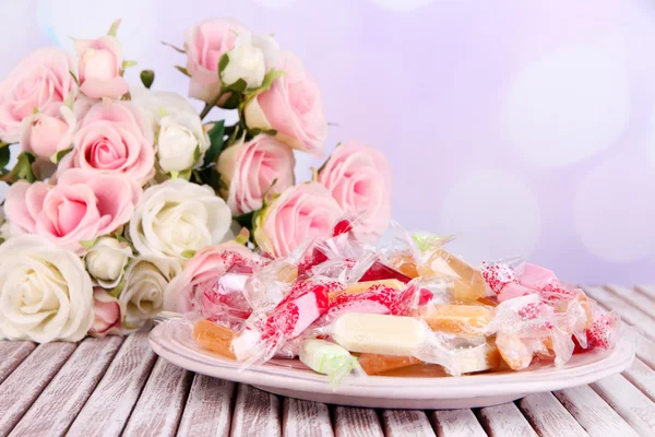 Tasty candies on plate with flowers on table on bright background