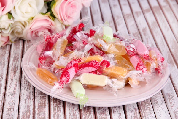 Вкусные конфеты на тарелке с цветами на деревянном фоне — стоковое фото