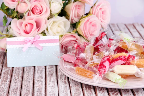 Lekkere snoepjes op plaat met bloemen en kaart op tafel op lichte achtergrond — Stockfoto