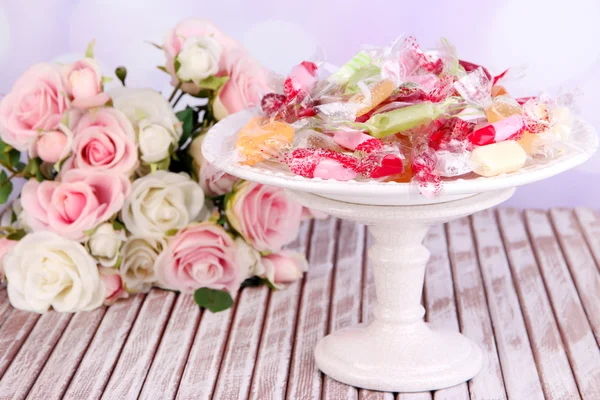 Sabrosos caramelos en plato con flores en la mesa sobre fondo brillante — Foto de Stock