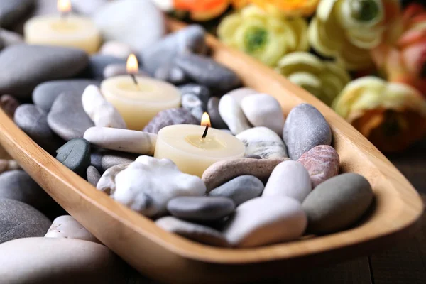 Tigela de madeira com pedras de spa e velas na mesa de madeira, no fundo flores — Fotografia de Stock