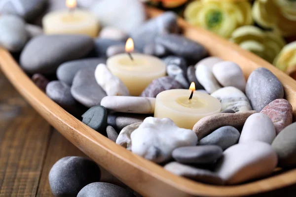 Drewniana miska spa kamienie i świece na drewnianym stole, na tle kwiatów — Zdjęcie stockowe