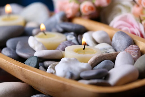 Wooden bowl with spa stones and candles on wooden  table, on flowers background — Stock Photo, Image