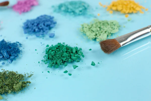 Arco iris triturado sombra de ojos y maquillaje profesional cepillo sobre fondo azul —  Fotos de Stock