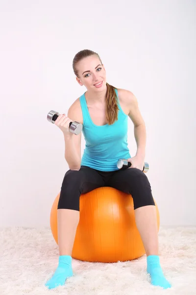 Young beautiful fitness girl exercising with orange ball and dumbbells in gym — Stock Photo, Image