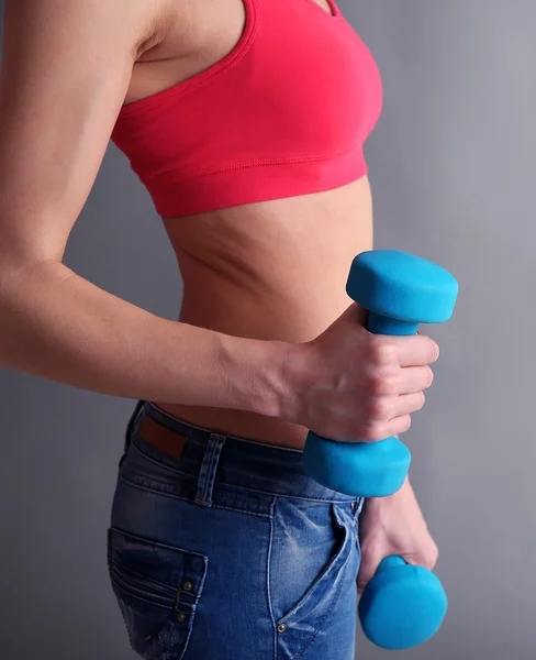 Jonge mooie fitness meisje uitoefenend met halters, close-up, op grijze achtergrond — Stockfoto