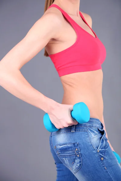 Joven hermosa chica de fitness haciendo ejercicio con pesas, primer plano, sobre fondo gris — Foto de Stock