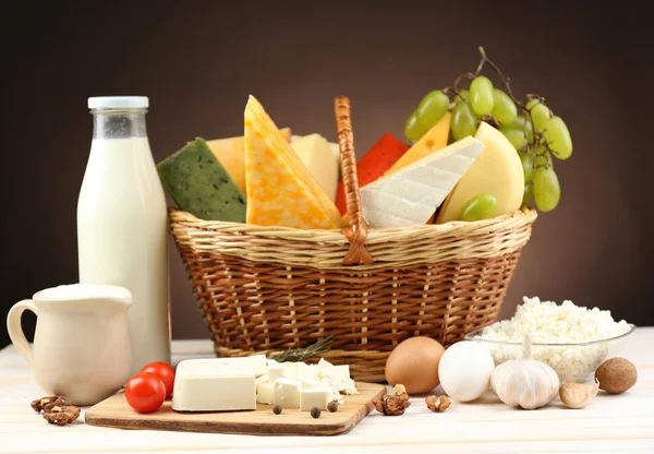 Basket with tasty dairy products on wooden table, on dark brown background — Stock Photo, Image