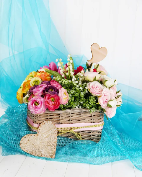 Bellissimi fiori in cesto di vimini, su tessuto a colori e sfondo in legno — Foto Stock