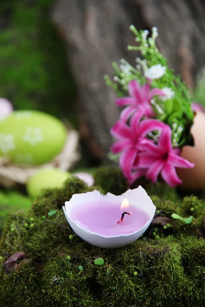 Composição conceitual da Páscoa. Vela ardente em ovo, ovos de Páscoa e flores no fundo de grama verde, close-up — Fotografia de Stock