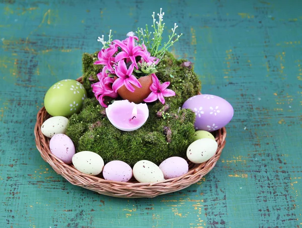 Composition conceptuelle de Pâques. Bougie brûlante dans l'oeuf, oeufs de Pâques, et des fleurs sur la mousse décorative et tapis d'osier, sur fond en bois, gros plan — Photo