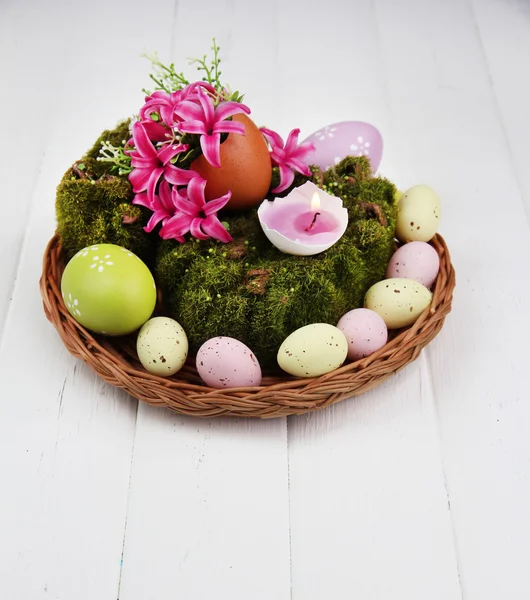 Composition conceptuelle de Pâques. Bougie brûlante dans l'oeuf, oeufs de Pâques, et des fleurs sur la mousse décorative et tapis d'osier, sur fond en bois, gros plan — Photo