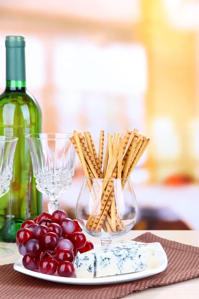 Cheese, grape and bread sticks on plate on wooden table, on bright background — Stock Photo, Image