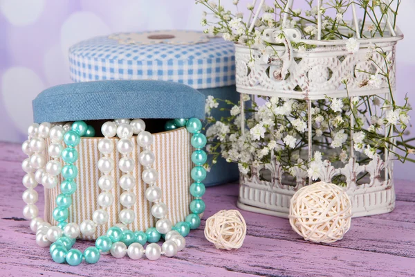 Decorative boxes with beads and flowers on table on bright background — Stock Photo, Image