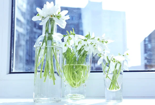 Beautiful bouquets of snowdrops in vases on windowsill — Stock Photo, Image