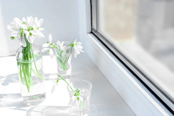 Beautiful bouquets of snowdrops in vases on windowsill — Stock Photo, Image