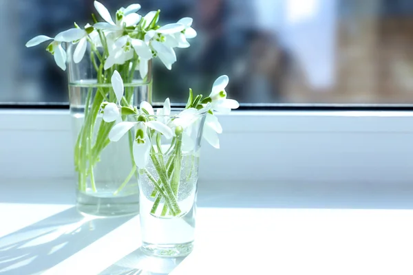 Beautiful bouquets of snowdrops in vases on windowsill — Stock Photo, Image