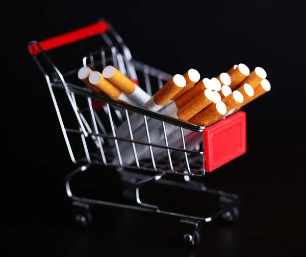 Cigarettes in shopping cart on wooden table on dark background — Stock Photo, Image