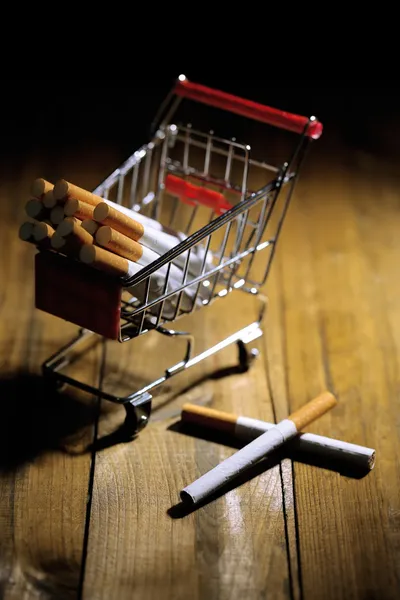 Cigarettes in shopping cart on wooden table on dark background — Stock Photo, Image