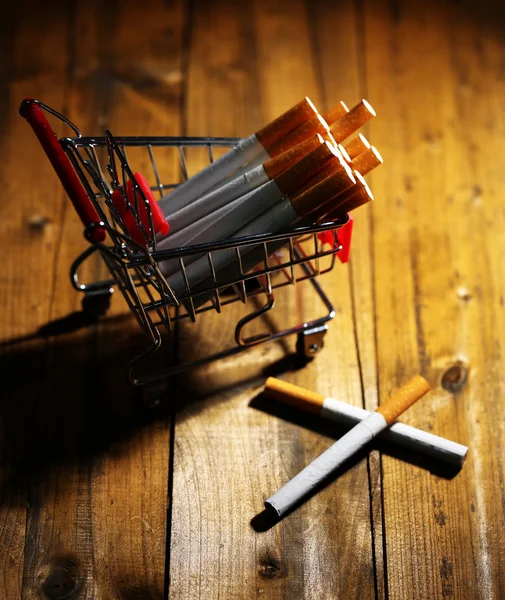 Cigarettes in shopping cart on wooden table on dark background — Stock Photo, Image