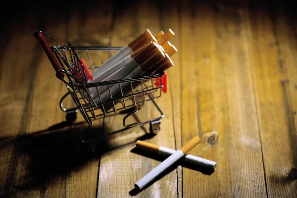 Cigarros no carrinho de compras na mesa de madeira no fundo escuro — Fotografia de Stock