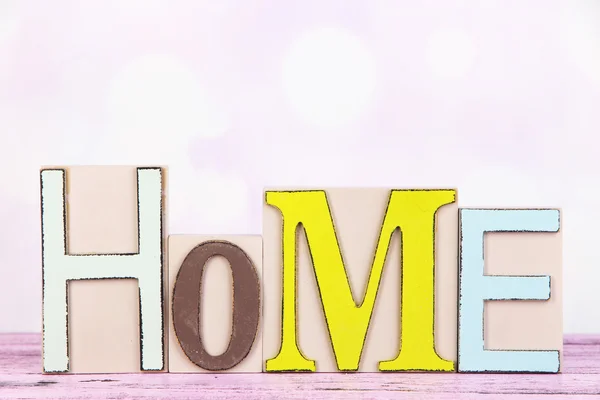 Letras decorativas formando palavra HOME na mesa sobre fundo brilhante — Fotografia de Stock