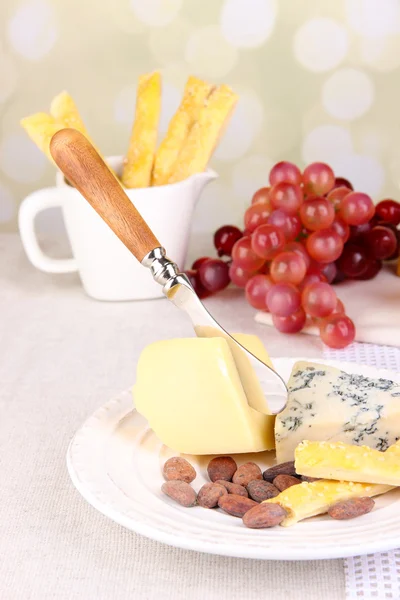 Placa de queso surtido, copa de uva y vino en la mesa, sobre fondo claro — Foto de Stock