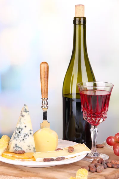 Piatto di formaggio assortito, uva e bicchiere di vino sul tavolo, su sfondo chiaro — Foto Stock